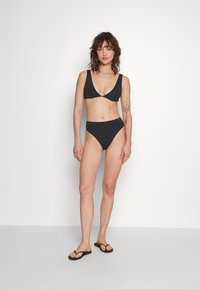 Svart bikini-set bestående av en triangulär bralette och högmidjade underdelar. Slät yta med breda band och minimalistisk design.