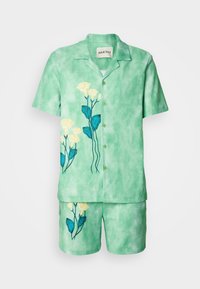 Grøn tie-dye sæt med kortærmet skjorte og shorts, der har broderede gule blomster og blå blade. Letvægts, afslappet design.