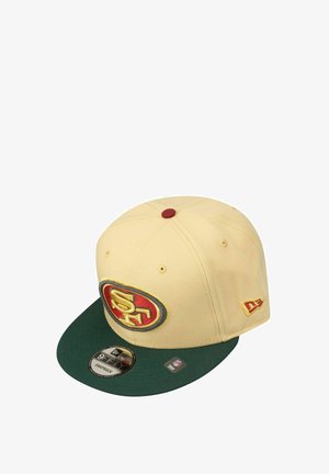 Cremfarbener Hut mit grünem Schild, mit einem gestickten Logo in Rot, Gelb und Schwarz. Enthält Belüftungslöcher und einen Snapback-Verschluss.