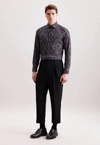 Donkere, lange mouwen overhemd met patroon en kraag, gecombineerd met hoge zwarte broek en zwarte veterschoenen. Eenvoudig, modern ontwerp.