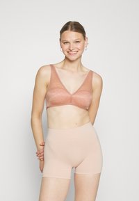 Hellrosa Spitzen-Bralette mit V-Ausschnitt und dünnen Trägern, kombiniert mit beigen nahtlosen Shorts, die eine glatte Textur aufweisen.