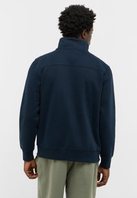 Felpa blu navy con colletto alto, polsini e fondo a costine. Tessuto morbido con un design semplice e pulito, caratterizzato da una cucitura orizzontale sul retro.