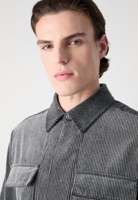 Black and gray striped shirt with a button-down collar, featuring two chest pockets and a textured fabric.