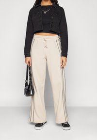 Zkrácená černá denimová bunda, přiléhavý černý top, béžové široké kalhoty s černými bočními pruhy, černá kabelka a černé tenisky.