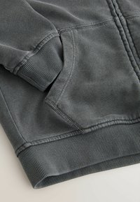 Grå sweatshirt med tekstureret stof, der har ribbede manchetter og kant, synlige syninger og en forlommer.