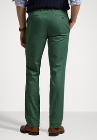 Gröna bomullsbyxor med slim fit, utrustade med fickor med knappstängning och en mjuk textur, kombinerade med bruna skor.