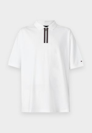 Valkoinen polo-paita, jossa on musta ja punainen raidallinen nappilista. Lyhyet hihat, pehmeä puuvillakangas ja logo vasemmassa hihassa.