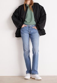 Musta pehmustettu bomber-takki, vihreä neule, vaaleansiniset suorat farkut ja valkoiset lenkkarit. Yksinkertainen muotoilu, klassinen istuvuus.