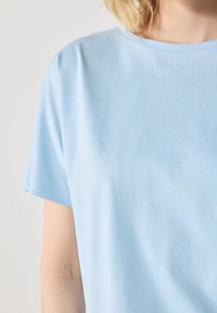 Lyseblå bomull T-skjorte med rund hals og korte ermer. Stoffet ser glatt ut med en subtil tekstur.