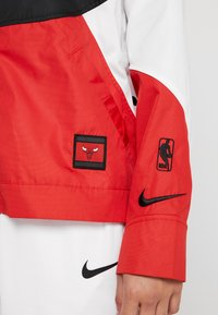 Röd och vit lätt jacka med svarta accenter. Har en Bulls-logotyp påärmen och NBA-logotypen. Tillverkad av slitstark tyg.