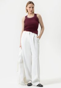 Débardeur bordeaux côtelé avec bord en dentelle, associé à un pantalon large blanc taille haute. Chaussures noires à enfiler avec des clous métalliques.