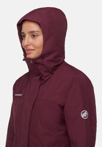 Bordowa wodoodporna kurtka z kapturem, z zatrzaskami i ściągaczem, oraz naszywką z logo na rękawie. Gładka tekstura.