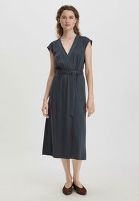 Mekko tummanharmaasta kankaasta, lyhyet cap-satavat hihat, syvä V-pääntie, vyötärölle kiristetty vyö, valuva muoto, polvipituinen, sileä rakenne, yhdistetty ruskeiden kenkien kanssa.