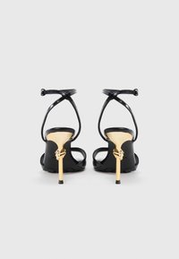 Sandalias negras de tacón alto con tiras finas, un tacón en tono dorado con un acento de nudo y una textura suave. Diseño de parte trasera abierta.
