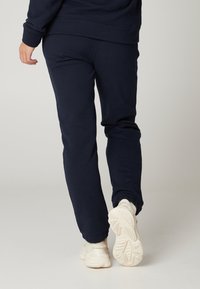 Námořnické modré joggingové kalhoty vyrobené z měkké tkaniny, s mírně zúženým střihem. Spárovány s bílými sportovními botami s texturovanou podrážkou.