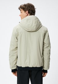 Lichtbeige hoodie met ritssluiting, elastische manchetten en een getailleerde zoom. De stof lijkt glad en licht glanzend.