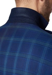 Niebieska koszula w kratę z wyraźnym kołnierzykiem, miękką fakturą i wzorem w kratkę w różnych odcieniach niebieskiego i zielonego.