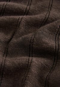 Tissu tricoté brun foncé avec une texture côtelée verticale et des coutures visibles, montrant des plis doux et des fibres de fil détaillées.