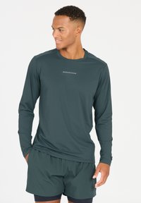 Langärmliges Sportshirt aus dunkelgrünem Stoff mit glatter Textur. Verfügt über einen runden Ausschnitt und ein dezentes "ENDURANCE"-Logo auf der Brust.