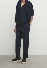 Navy short-sleeve sweater with a knitted texture, paired with loose-fitting navy trousers and dark sneakers with light soles.