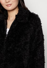 Svart konstläderjacka med en texturerad yta, med dragkedja fram och krage. Mjuk och fluffig material.
