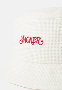 Fehér, texturált anyagból készült vödrös sapka, az elején piros hímzett "JACKER" felirattal. Enyhe ívű karima, varrás nélküli dizájn.