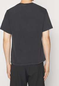 Camiseta de manga corta en algodón gris oscuro, con cuello redondo y corte relajado, con un dobladillo sencillo y sin marcas visibles.