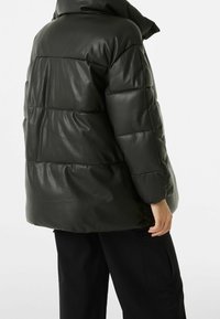 Tmavě zelená prošívaná bunda z lesklého syntetického materiálu, s vysokým límcem a prošívanými částmi; doplněná o černé kalhoty.