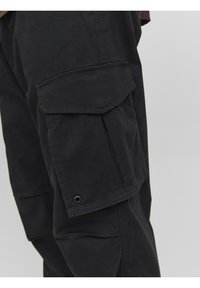 Svarta cargobyxor i bomullsmaterial, med en stor sidficka, sydda sömmar och en tryckknappdetalj.