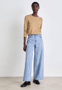 Suéter marrón claro, jeans de pierna ancha azul claro y mocasines negros. El suéter tiene mangas largas; los jeans presentan una cintura alta y un corte recto.