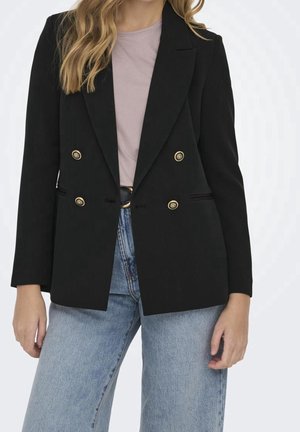 Vrouw draagt een zwarte double-breasted blazer met gouden knopen, lichtpaarse top, blauwe spijkerbroek en een zwarte riem.