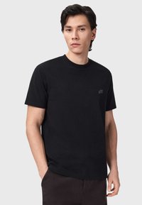 Μαύρο βαμβακερό t-shirt με στρογγυλή λαιμόκοψη, κοντά μανίκια και διακριτικό λογότυπο στο στήθος. Λεία υφή και κλασική εφαρμογή.