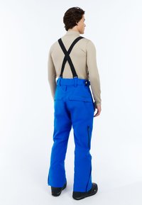 Blauwe sneeuwbroek met afneembare zwarte bretels, ritszakken en versterkte zoom. Gemaakt van duurzaam, weerbestendig materiaal.