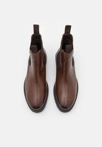 Botines de cuero marrón con paneles laterales elásticos, puntera redondeada y lengüetas para facilitar el calzado. Textura suave y brillante con suela contrastante.