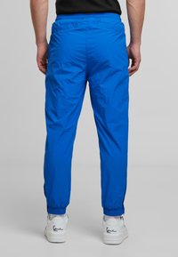 Blue elastic-waist joggers with a smooth texture, tapered cuffs, and two back pockets. Worn with white sneakers featuring black accents.