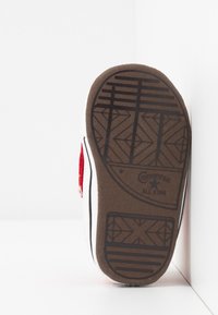 Converse All Star sneakersål, brun gummi med struktureret grebmønster, hvid canvas overdel, røde stofdetaljer på siden.