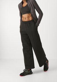 Svarta byxor med vida ben och dragsko i midjan, kombinerade med en mörk atletisk topp och svarta sneakers med röda accenter. Sl ät, tygtextur.