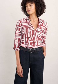 Camisa a rayas rojas y blancas con cuello de muesca, combinada con pantalones de mezclilla oscuros y un cinturón negro con una hebilla redonda de plata.