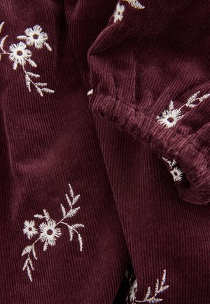 Bordo spalvos korduro audinys su baltais gėlių siuvinėjimais; elastinės rankogaliai ir subtilūs lapų raštai suteikia papildomą tekstūrą ir detales.