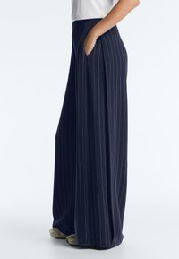 Person wearing navy blue wide-leg pinstripe trousers with hand in pocket, paired with white top and beige shoes.