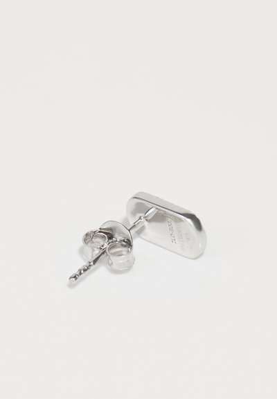 Ασημένιο μεταλλικό σκουλαρίκι με οβάλ σχέδιο, που διαθέτει ορατό κλείσιμο στο πίσω μέρος και λεπτομέρειες στην επιφάνεια.