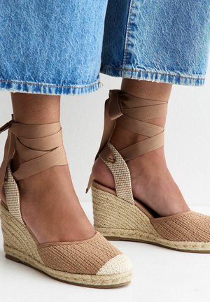 Wedges met geweven beige bovenwerk en crèmekleurige neus, enkellintjes, gedragen met cropped lichtblauwe spijkerbroeken.