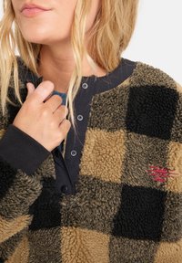 Bruine en zwarte geruite fleece pullover met een knoopsluiting bij de kraag, met een zachte textuur en een rood logo op de borst.