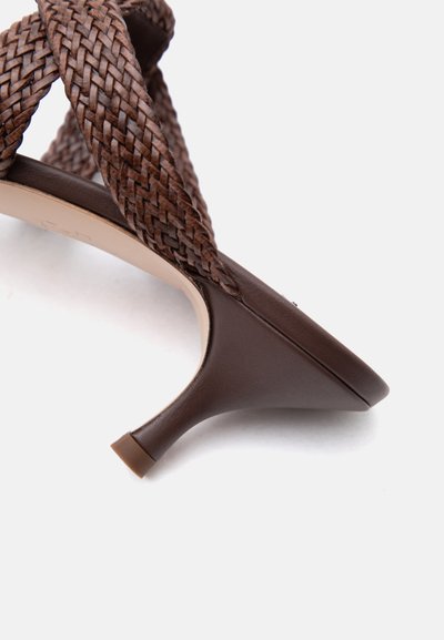 Καφέ δερμάτινο σανδάλι με τακούνι τύπου kitten, με πλεκτές λουράκια που διασταυρώνονται και μυτερή μύτη, σε λευκό φόντο.