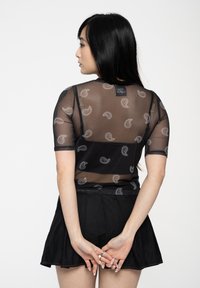 Black short-sleeve top with sheer fabric and paisley pattern details. Paired with a black flared skirt, showcasing a layered design.