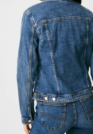 Chaqueta de mezclilla en azul medio, con un diseño clásico, textura suave, costuras visibles y botones a presión metálicos en la cintura.