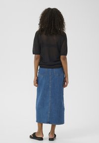Top noir à manches courtes associé à une longue jupe en denim bleu avec poches latérales et un ourlet légèrement usé. Sandales noires minimalistes.