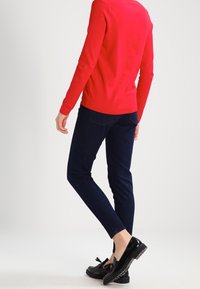 Punainen pitkähihaisen neule, tummansiniset slim-fit farkut ja mustat loafersit, joissa on sulkavihrian yksityiskohta. Silkkinen rakenne, istuva muotoilu ja minimalistic tyyli.