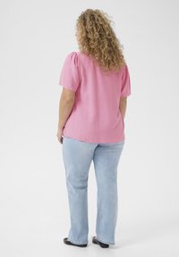 Blusa rosa a maniche corte con finitura testurizzata e cuciture delle spalle arricciate, abbinata a jeans dritti blu chiaro e ballerine nere.