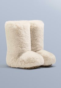 Beige, pluizige bontlaarzen met een zachte textuur, een afgeronde neus en een korte hoogte, voorzien van een lichte rubberen zool voor binnenshuis gebruik.